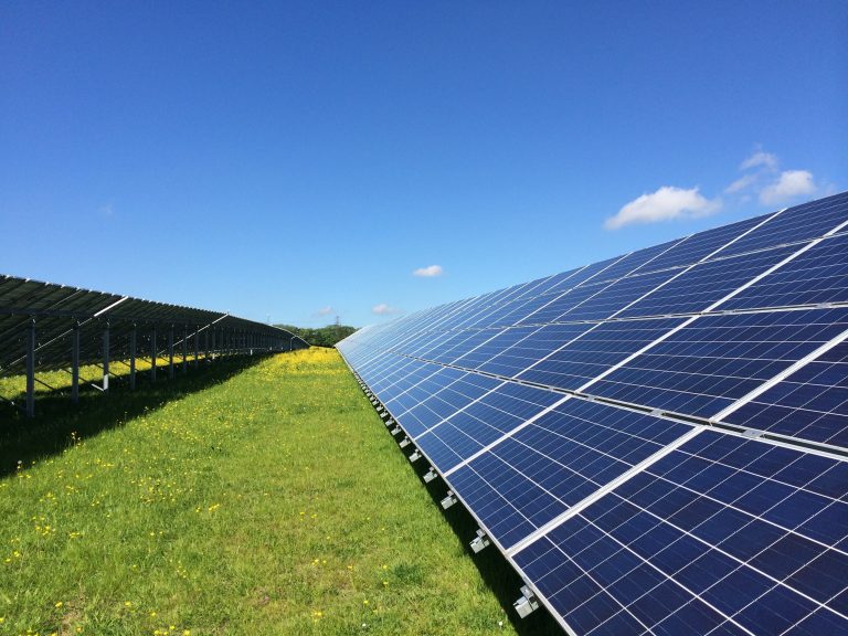 A row of solar panels in a green field, with blue sky above